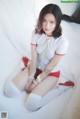 A woman in a white shirt and red shorts sitting on a bed.