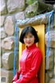 A woman in a red dress leaning against a stone wall.