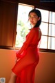 A woman in a red dress standing by a window.