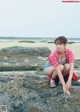 A woman sitting on top of a large rock on a beach.