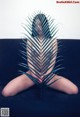 A naked woman sitting on a couch with a palm leaf in front of her.