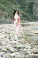 A woman in a pink kimono standing on a rocky beach.