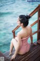 A woman in a pink bathing suit sitting on a wooden dock.