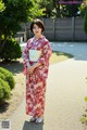 A woman in a red and white kimono standing in a garden.