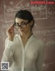 A woman wearing glasses standing in front of a blackboard.