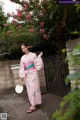 A woman in a pink kimono standing in front of a gate.