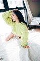 A woman sitting on a bed wearing a green sweater.