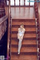 A woman in a white bodysuit sitting on a wooden staircase.