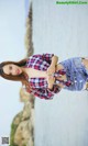 A woman in a plaid shirt and denim shorts posing by the water.