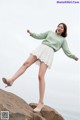 A woman in a green sweater and white skirt posing on a rock.