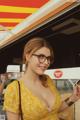 A woman in a yellow dress and glasses standing in front of a food truck.