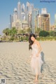 A woman in a white dress walking on a sandy beach.