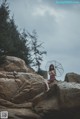 A woman sitting on a rock holding an umbrella.