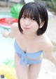 A woman in a blue bikini standing next to a pool.