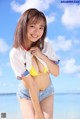 A woman in a yellow bikini standing on a beach.