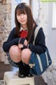 A young woman in a school uniform sitting on a stool.