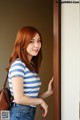 A woman in a blue and white striped shirt and jeans leaning against a wall.