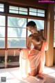 A naked woman sitting on a bed in front of a window.